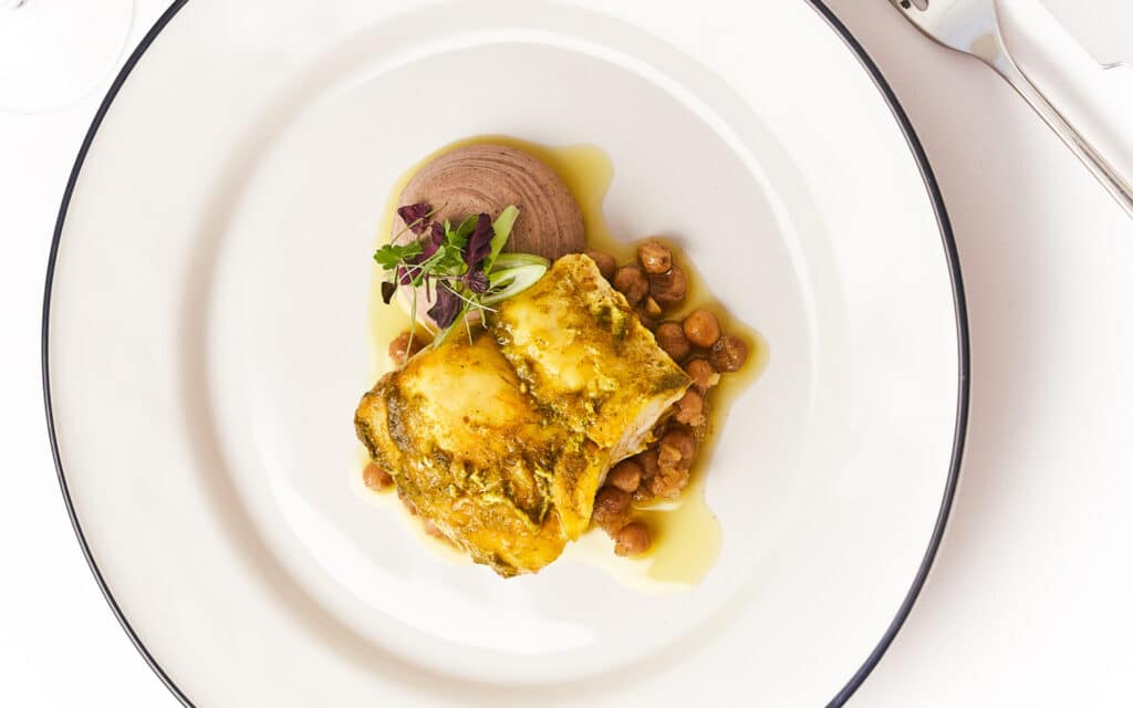 Chermoula Hake with Sumac hummus, Preserved Lemon, Chickpeas & Spiced Raisins as served in Tramonto restaurant.