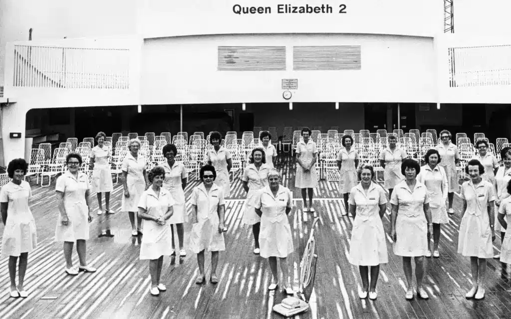 Housekeeping staff pose with a vacuum cleaner on board the QE2 ocean liner.