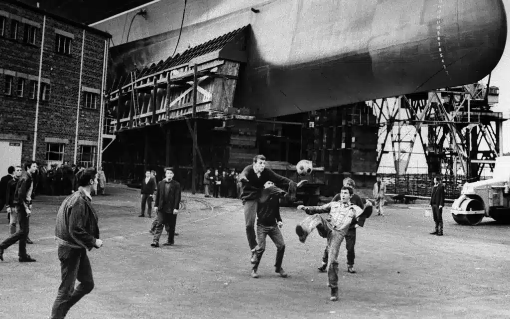 Ship builders play football beneath the keel of a Cunard liner.