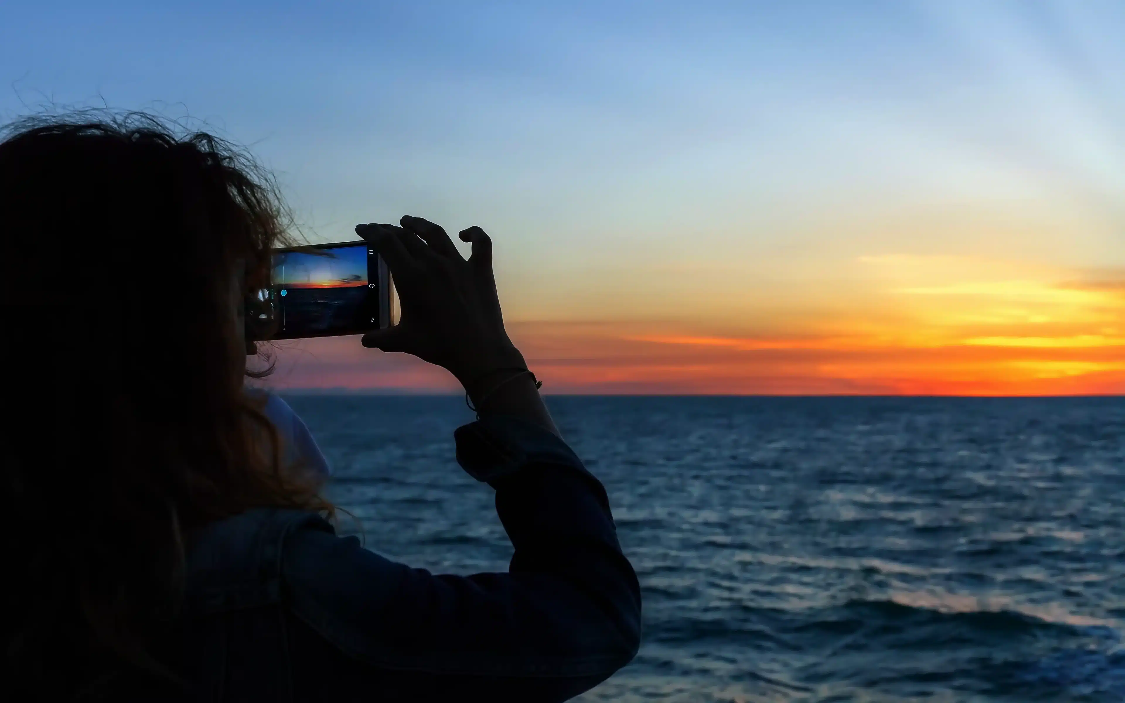 A female photographs sunset over the ocean.