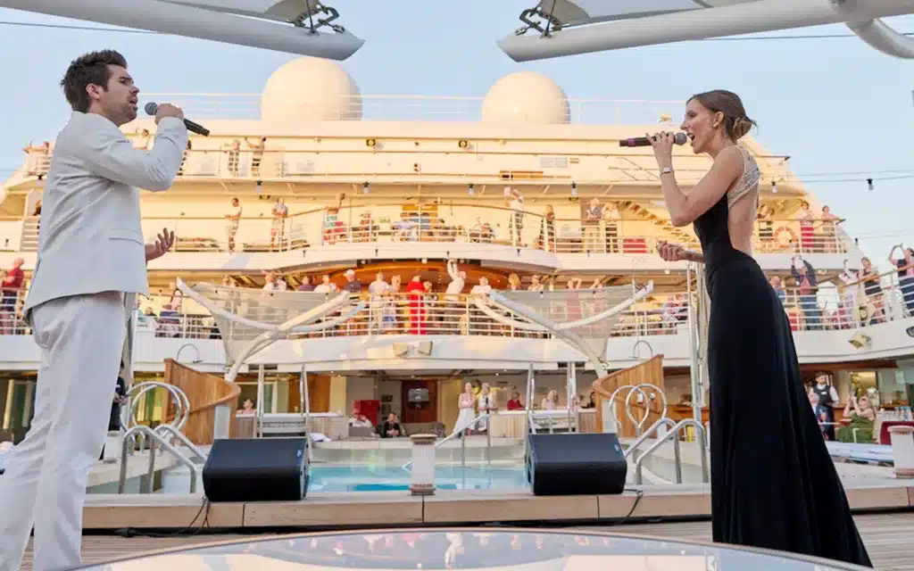 A male and female singer perform on the pool deck of a Seabourn ship.