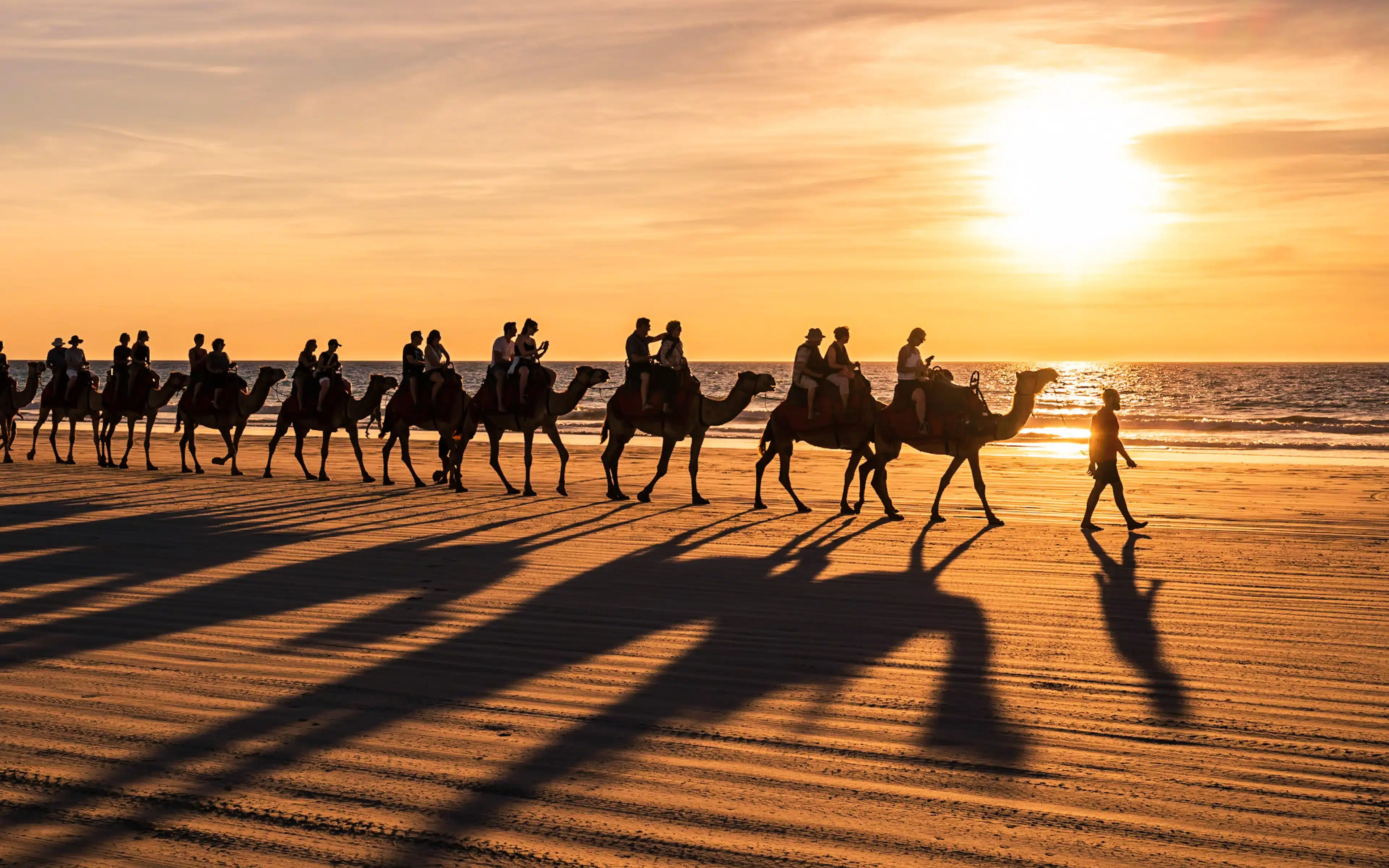 A group of riders on camels at sunset on Camble Beach, Australia. A destinatin for the Seabourn World Cruise 2027.