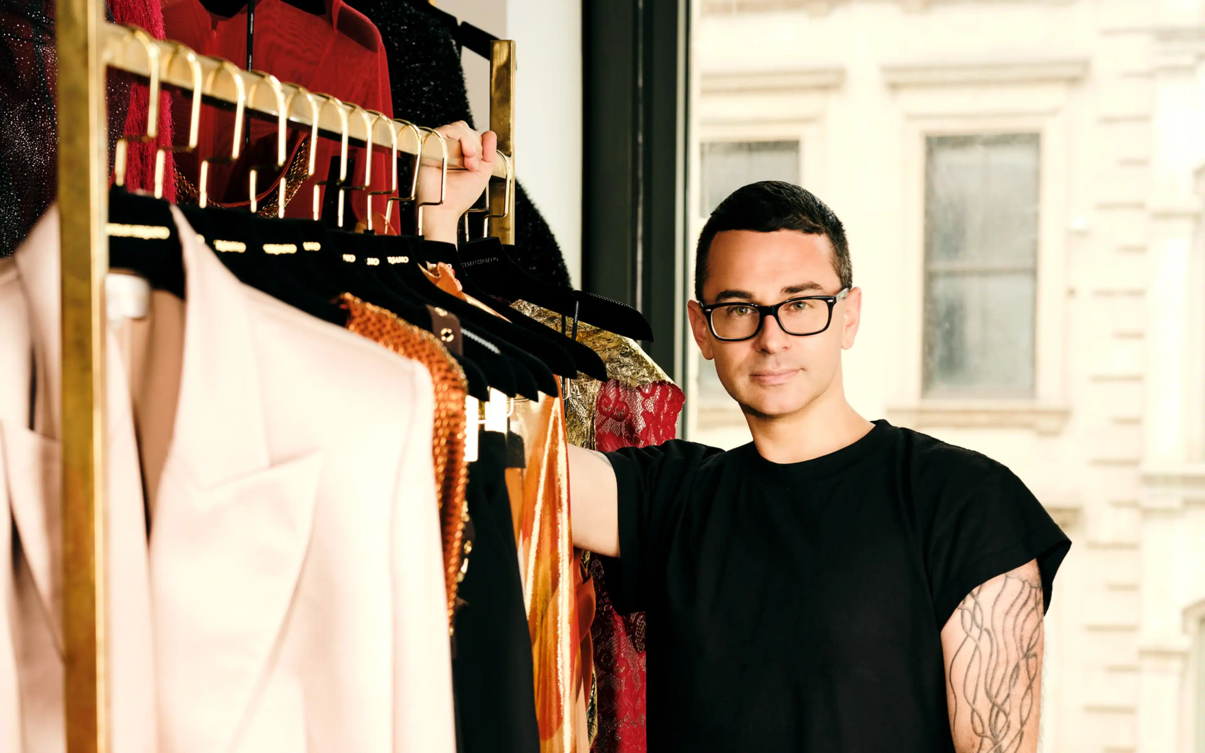 Christian Siriano posing next to a rack of designer clothes. (Photo: Shane LaVancher)