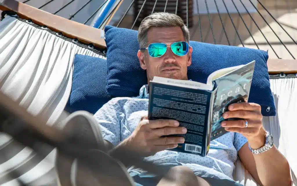 A male reading a book in a hammock.