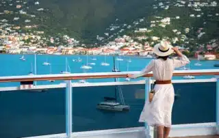 A pretty female stands on a cruise ship deck, looking out to sea.