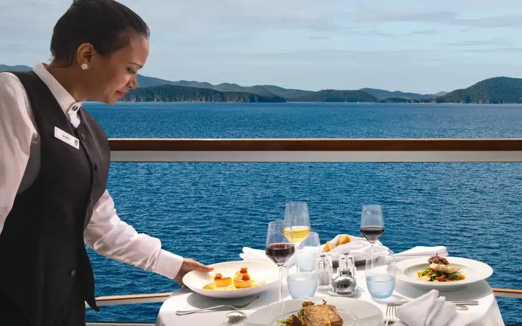 A suite host serves breakfast on a cruise ship balcony.