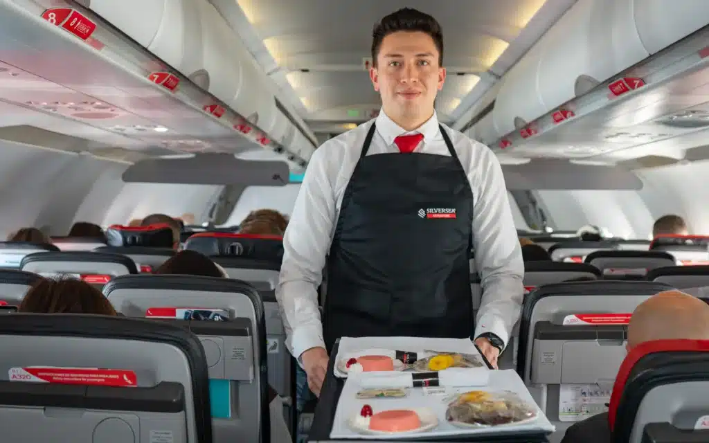 A male flight attendant with food trays on top of a trolly.