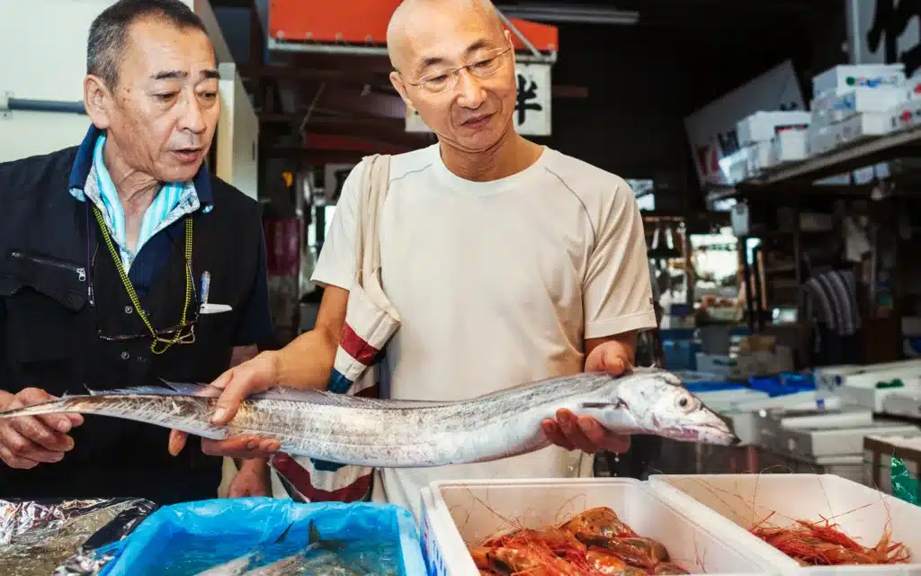 Two men, a seller and buyer, holding a long fish for sale in a traditional fish market in Tokyo.