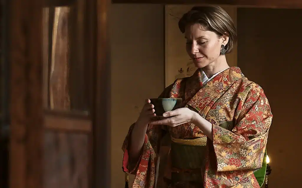 An elegant woman dressed in traditional Japanese attire holds a bowl of matcha tea.
