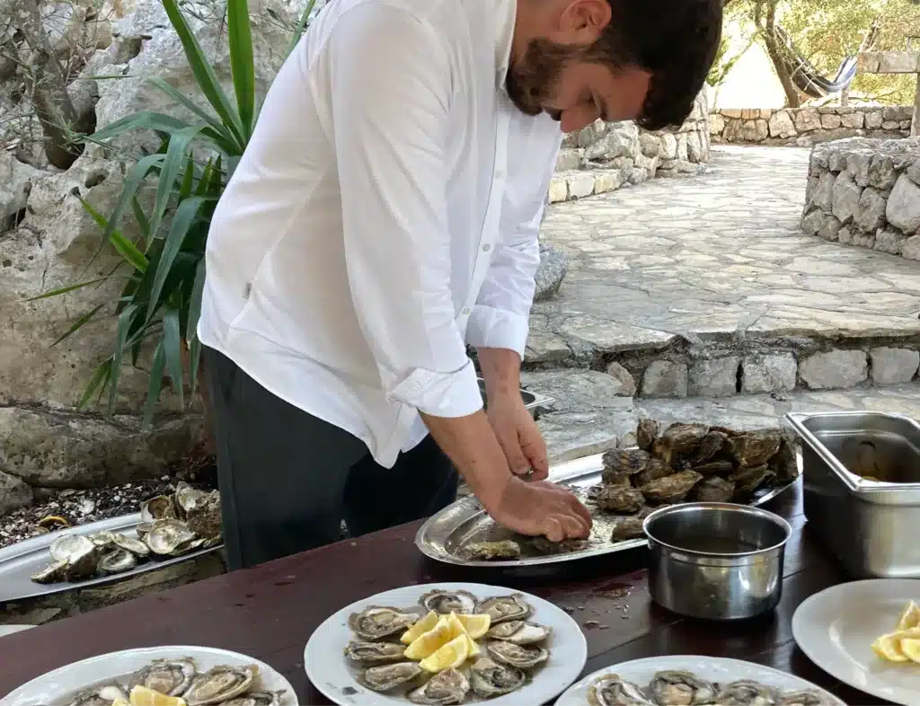A male shuckes fresh oysters on an outdoor table.