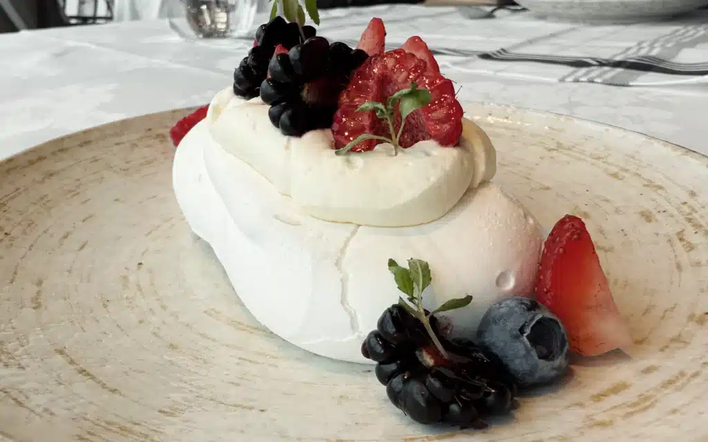 Pavlova topped with whipped cream and seasonal berries.
