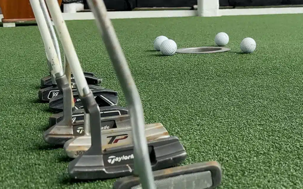 Close up on various golf putters with gold balls in the background.