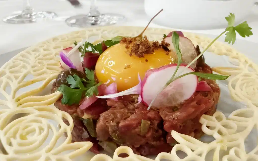 Beef Tartar with Black Garlic Aïoli, Confit Egg Yolk, Parmesan Tuile, and Anchovies.
