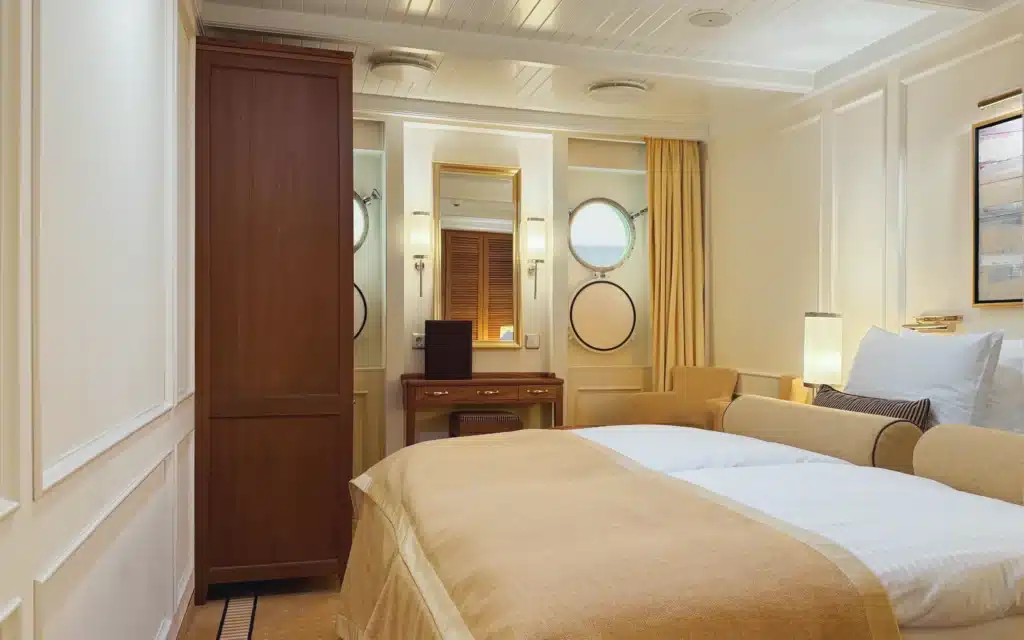 Sea Cloud Spirit Deluxe Stateroom with king bed, walnut joinery, brass portholes and warm cream décor