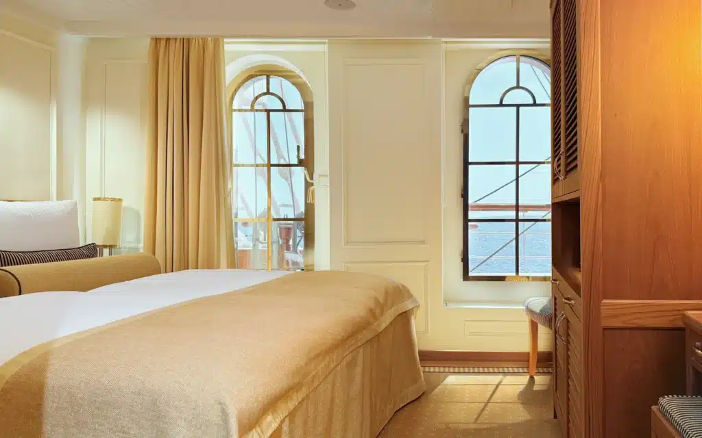 Sea Cloud Spirit Grand Stateroom with arched windows, king bed dressed in amber linens and warm cream paneled walls