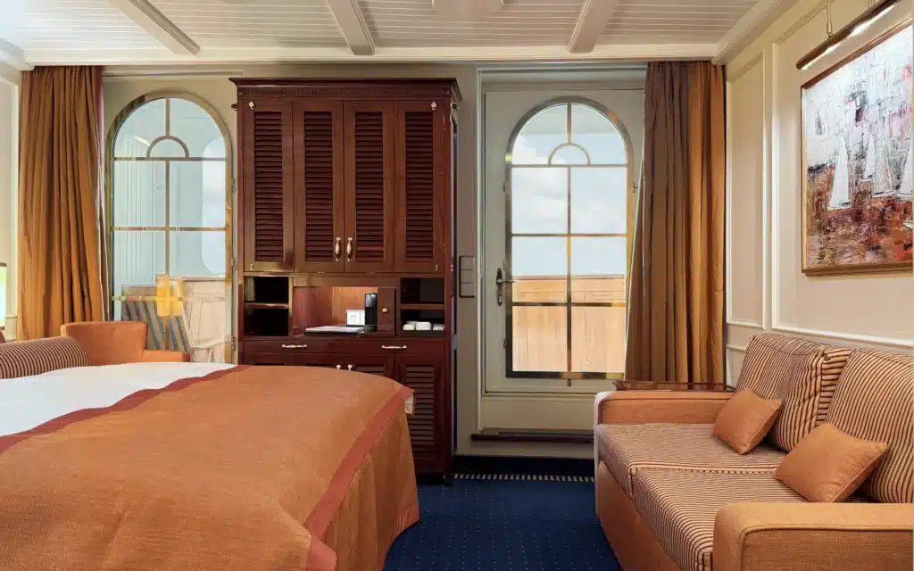 Sea Cloud Spirit Junior Veranda Suite showing the sitting area, striped sofa, mahogany storage and arched door to the private veranda