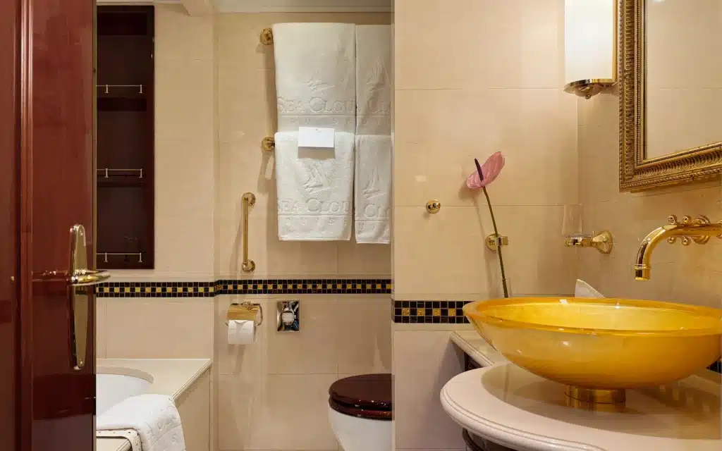 Sea Cloud Spirit Junior Veranda Suite bathroom with amber glass bowl basin, gold wall-mounted faucets, marble tiles and branded towels