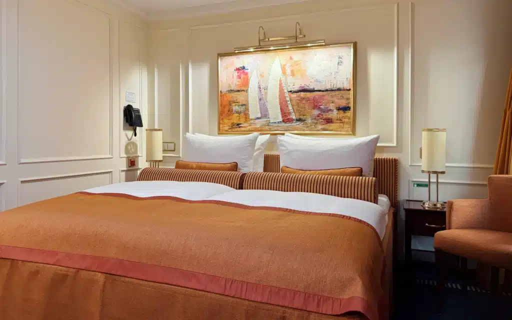 Sea Cloud Spirit Junior Veranda Suite king bed dressed in terracotta linens with striped cushions and a lit sailing artwork above the headboard