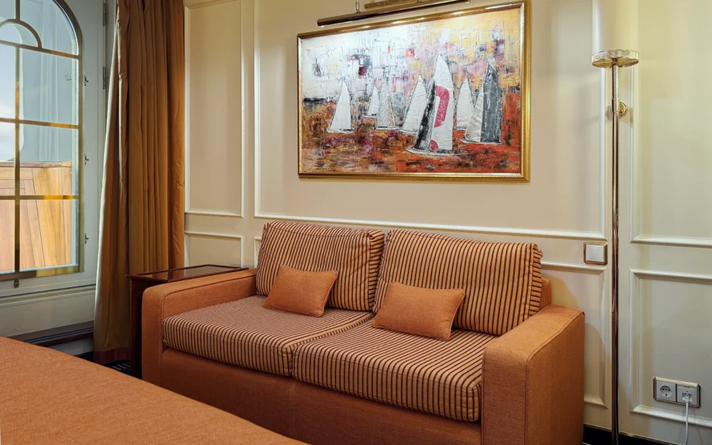 Sea Cloud Spirit Junior Veranda Suite sitting area with striped terracotta sofa, sailing fleet artwork and arched veranda window