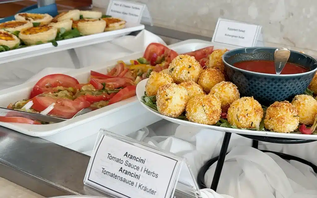 Sea Cloud Spirit Lido Bistro buffet showing golden arancini with tomato sauce, sliced tomato salad and ham and cheese tartlets