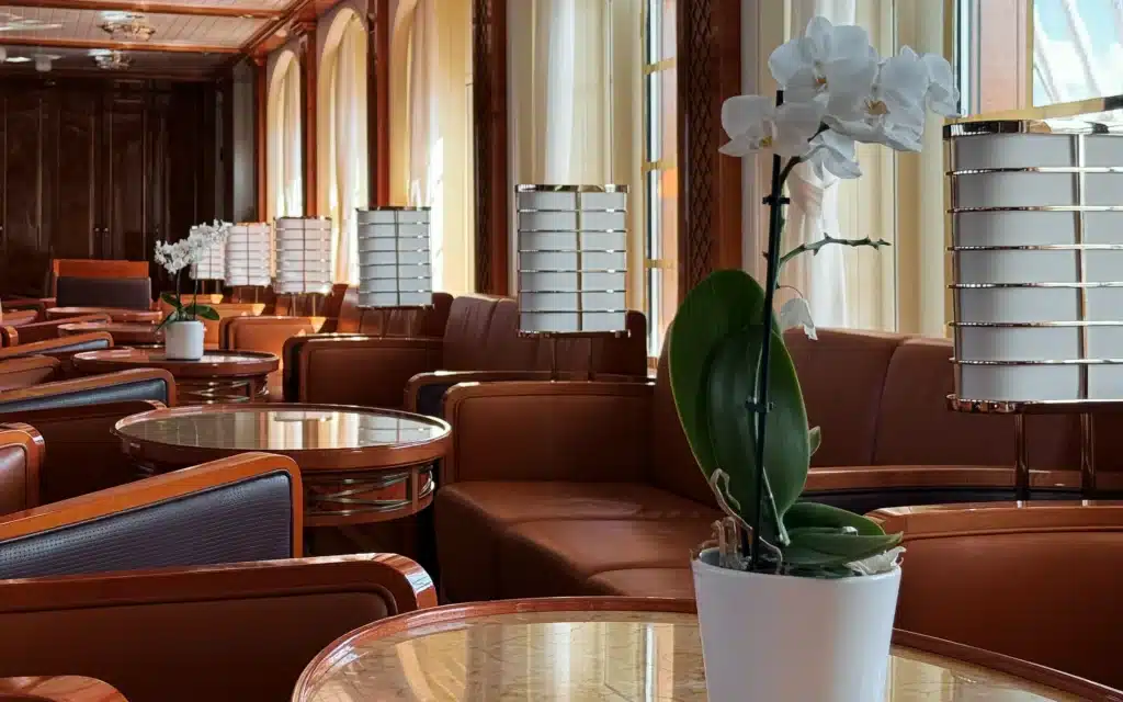 Sea Cloud Spirit main lounge with cognac leather club chairs, round marble-topped tables, white orchids and arched windows in warm afternoon light