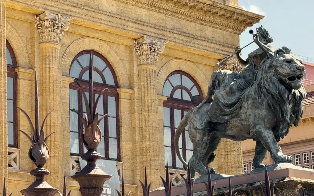 Bronze lion statue and ornate neoclassical facade of the Teatro Massimo opera house in Palermo, Sicily