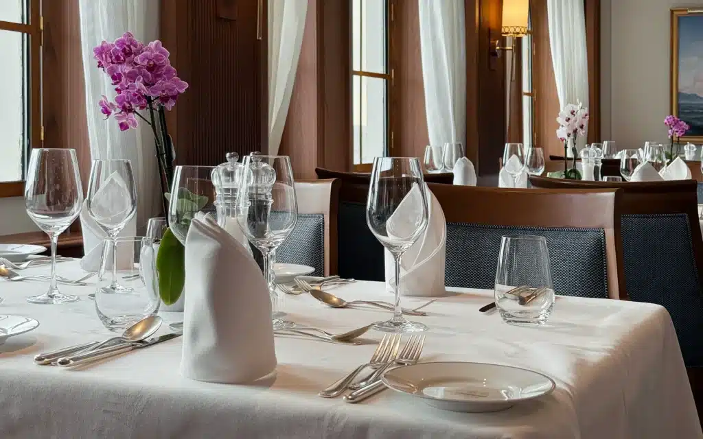 Sea Cloud Spirit main restaurant with white linen tablecloths, crystal stemware, silver cutlery, pink orchids and warm timber paneled walls