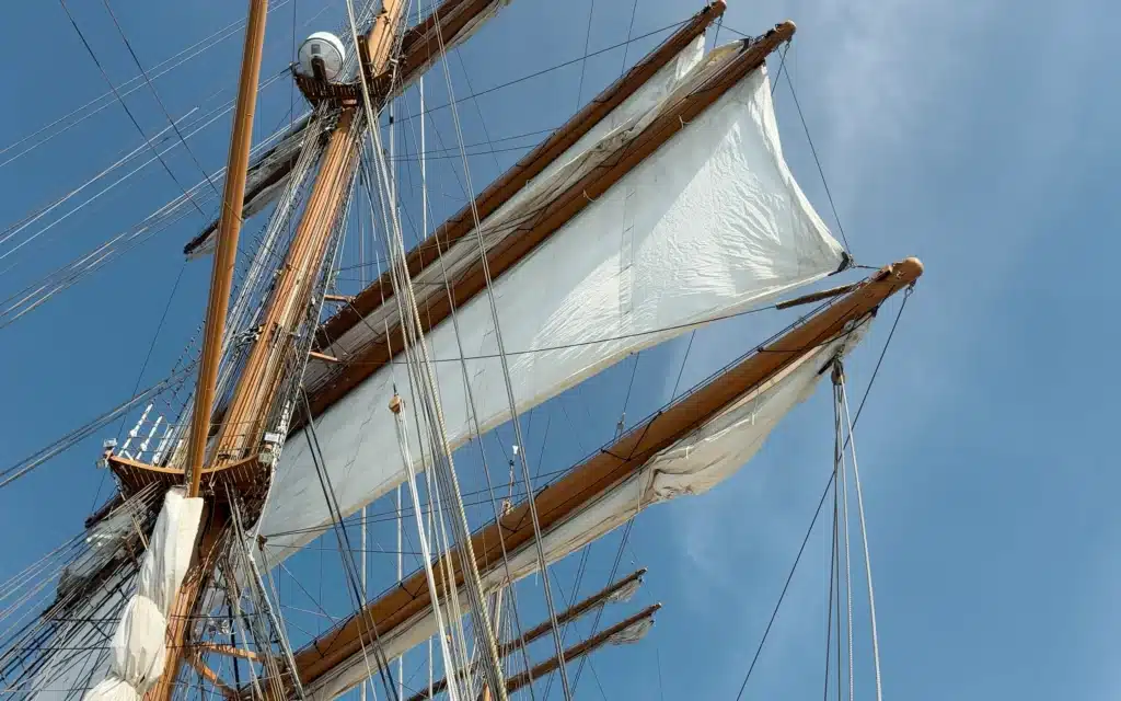 Upward view of Sea Cloud Spirit's square sails unfurling from the timber yards against a clear blue sky