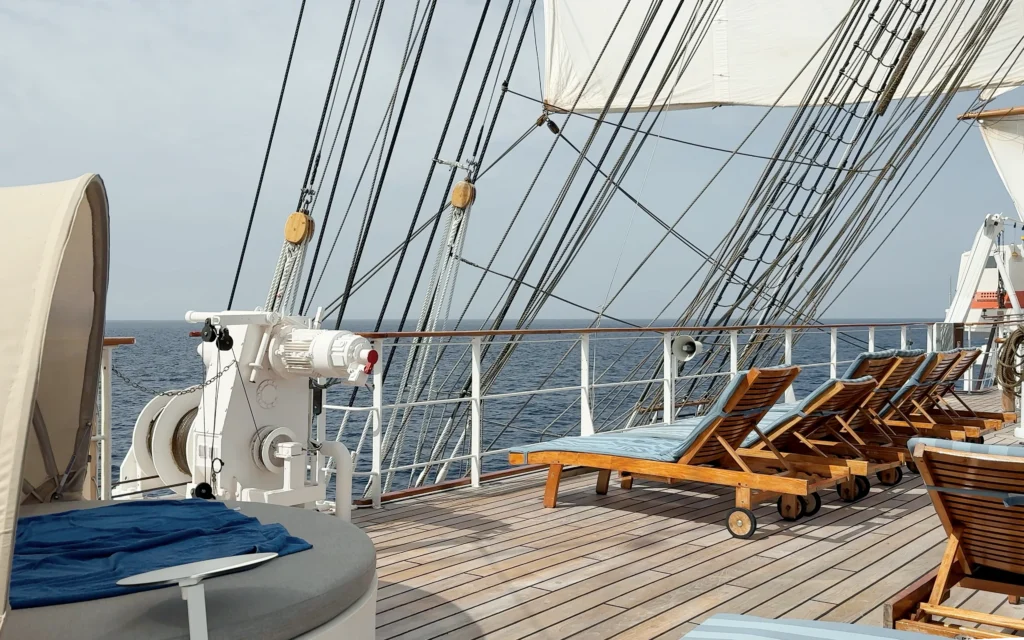 Sea Cloud Spirit sun deck with teak loungers and blue cushions along the rail, the ship's rigging and open ocean stretching to the horizon