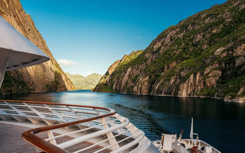 View from the bow deck of a SeaDream vessel as it navigates the steep rock walls of Trollfjord in northern Norway under a clear blue sky