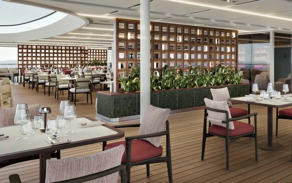 he open-air deck dining area of Osteria d'Ovidio on Crystal Grace, featuring teak timber decking, dark metal and woven chairs with burgundy cushions, set tables with glassware, a green tiled planter with tropical foliage, and illuminated wood lattice partitions
