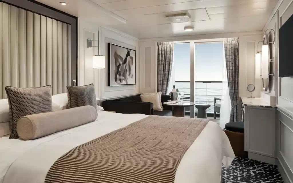 Oceania Marina Concierge Veranda Stateroom featuring a king bed with neutral upholstery, abstract wall art, a sitting area, and an open balcony with ocean views