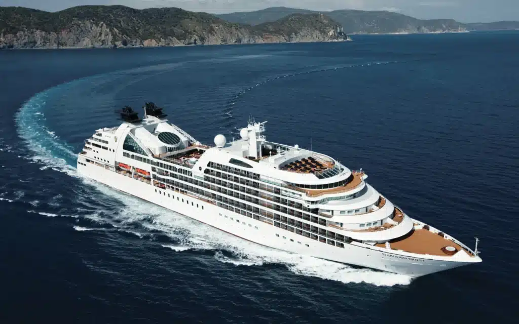 Aerial view of Seabourn Quest luxury cruise ship underway on deep blue waters with a forested coastline in the background
