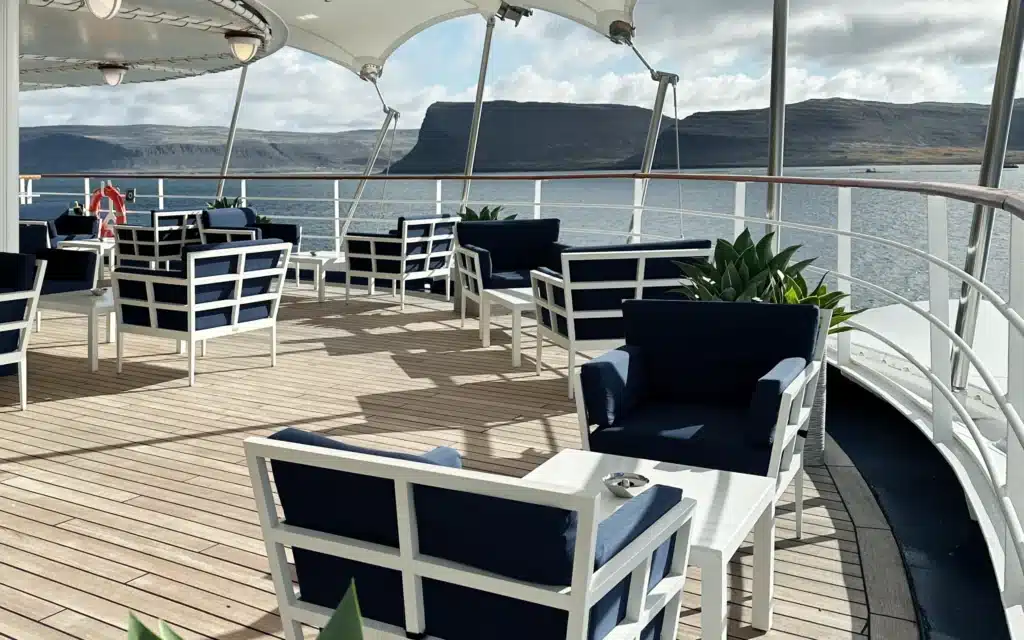 The Panorama Lounge terrace on Silver Spirit with navy-cushioned outdoor seating overlooking dramatic fjord cliffs
