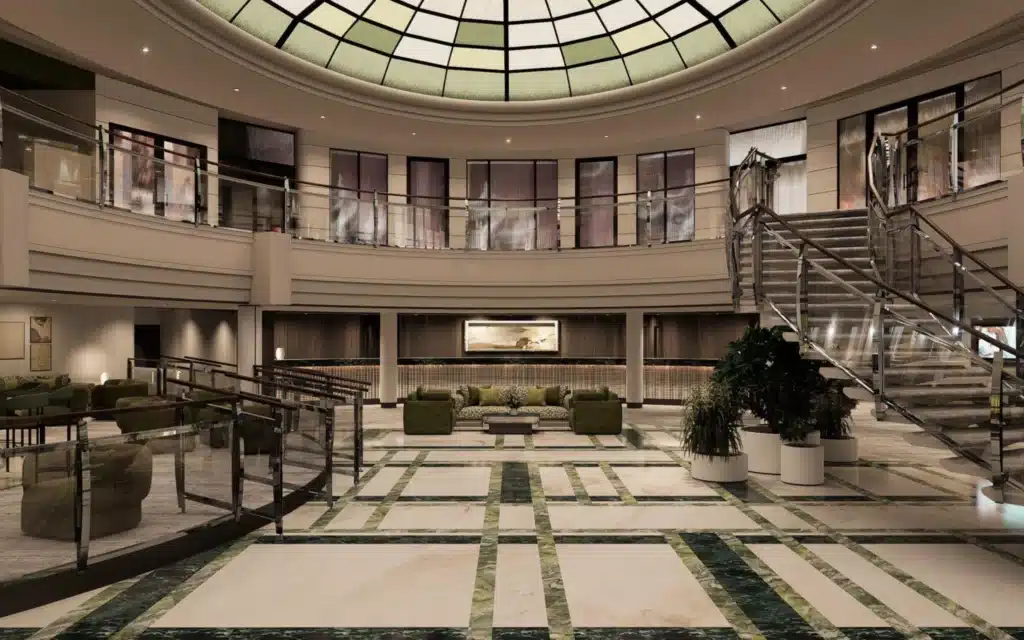 Grand atrium of Crystal Serenity following the 2026 drydock refit, viewed from the main floor toward a large circular stained-glass dome ceiling, with green and white inlaid marble flooring in a grid pattern, chrome and glass staircases to the right, a curved mezzanine balcony above, green velvet seating groupings, large potted tropical plants, and a framed landscape artwork illuminated above the reception desk in the background