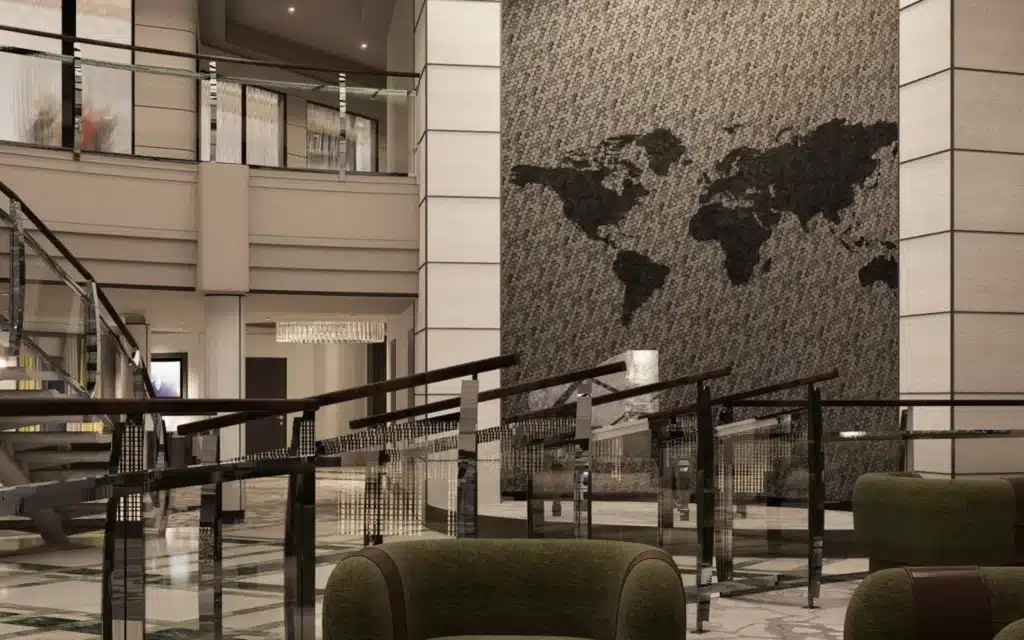 Multi-level atrium lobby of Crystal Serenity following the 2026 drydock refit, featuring a dramatic floor-to-ceiling hexagonal tile mosaic world map rendered in charcoal and light grey on the feature wall, glass-paneled balustrades with dark wood handrails on the mezzanine level, a crystal chandelier, polished marble flooring below, and deep green upholstered lounge seating in the foreground