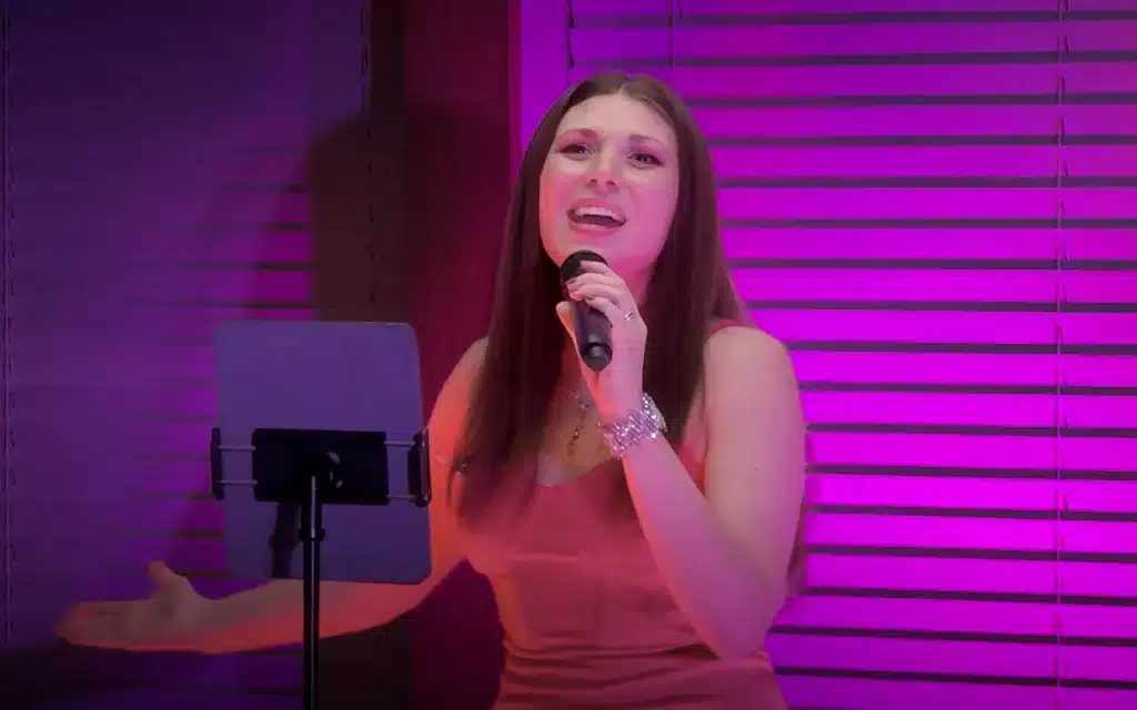 World Voyager onboard vocalist performing in the Dome Observation Lounge, singing expressively into a microphone in a red dress under vivid pink and magenta stage lighting