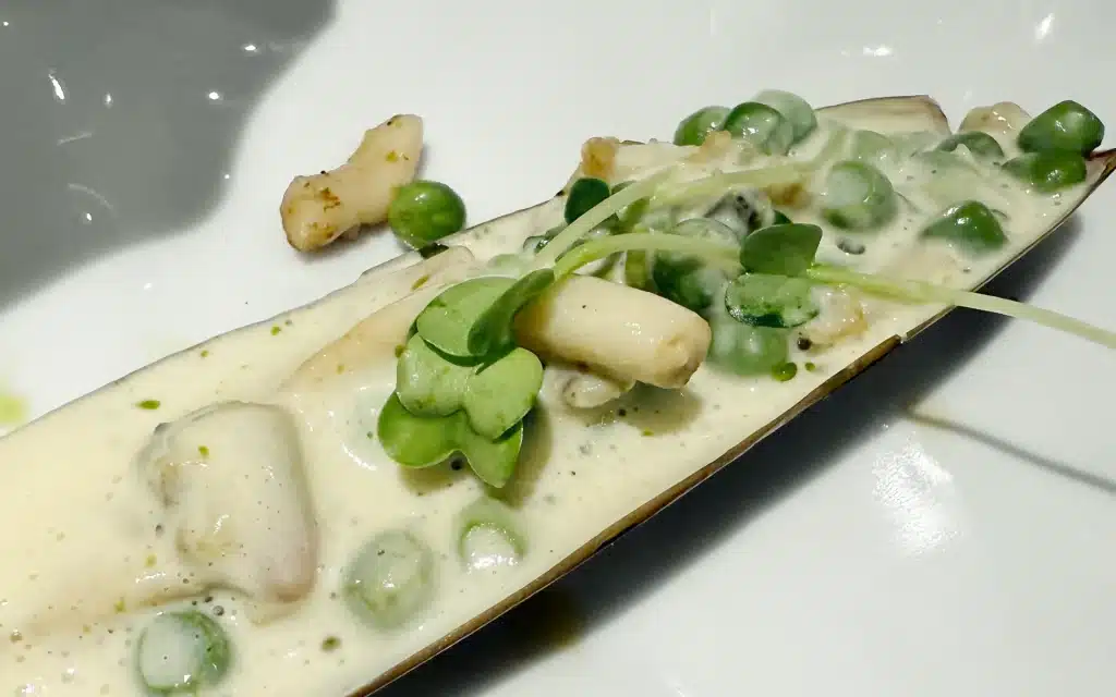 Madeira Restaurant razor clam dish with peas and asparagus in a cream sauce, served in the shell on a white rectangular plate with microgreens