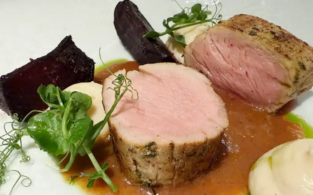 Madeira Restaurant veal tenderloin sliced to reveal a perfectly blush-pink interior, served with roasted beetroot, baby eggplant, microgreens, cream quenelles, and a glossy pan jus on a white plate