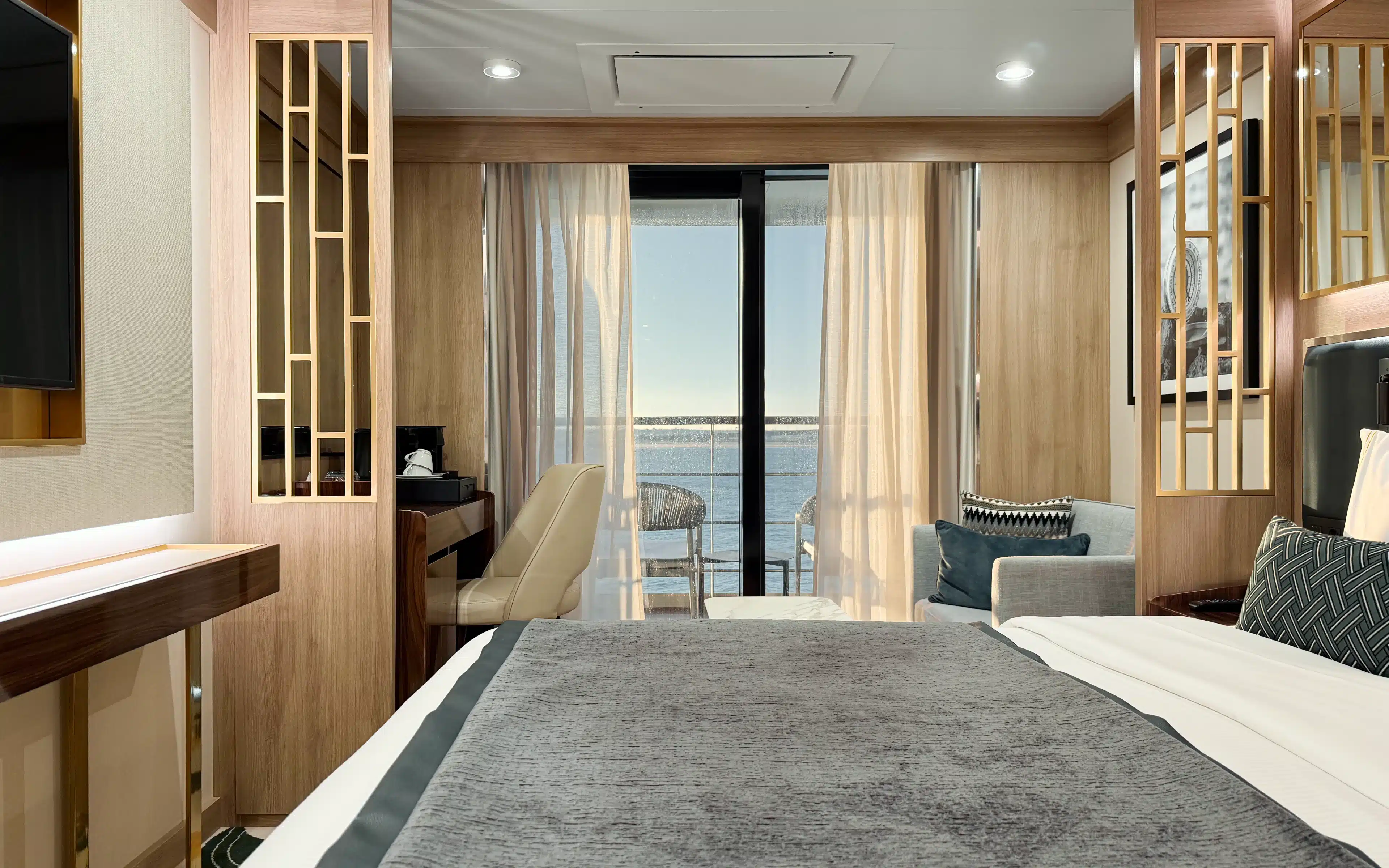 orld Voyager Veranda Suite bedroom bathed in warm afternoon light, with king bed, sitting area, and access to a private veranda