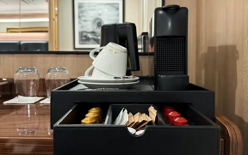 In-suite Nespresso coffee machine with leather capsule organizer, white cups and saucers, and wine glasses in a World Voyager Veranda Suite