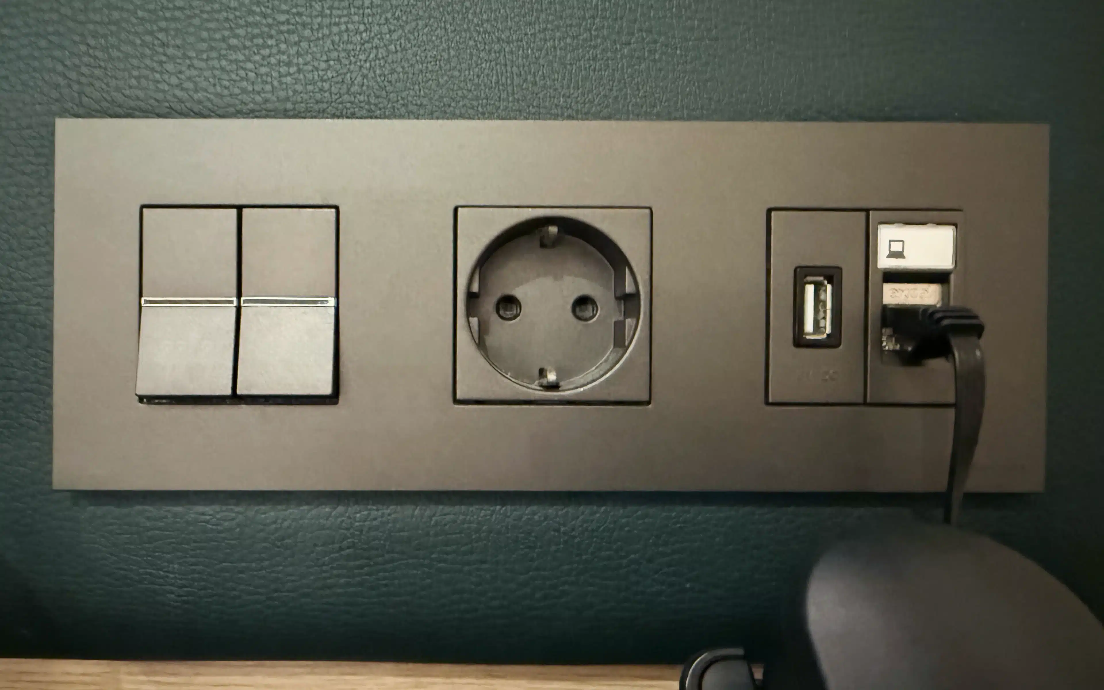 Bedside power panel in a World Voyager Veranda Suite featuring dual rocker switches, a European-style outlet, USB port, and ethernet connection