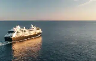 Azamara Pursuit small cruise ship sailing at sunset on calm open ocean.