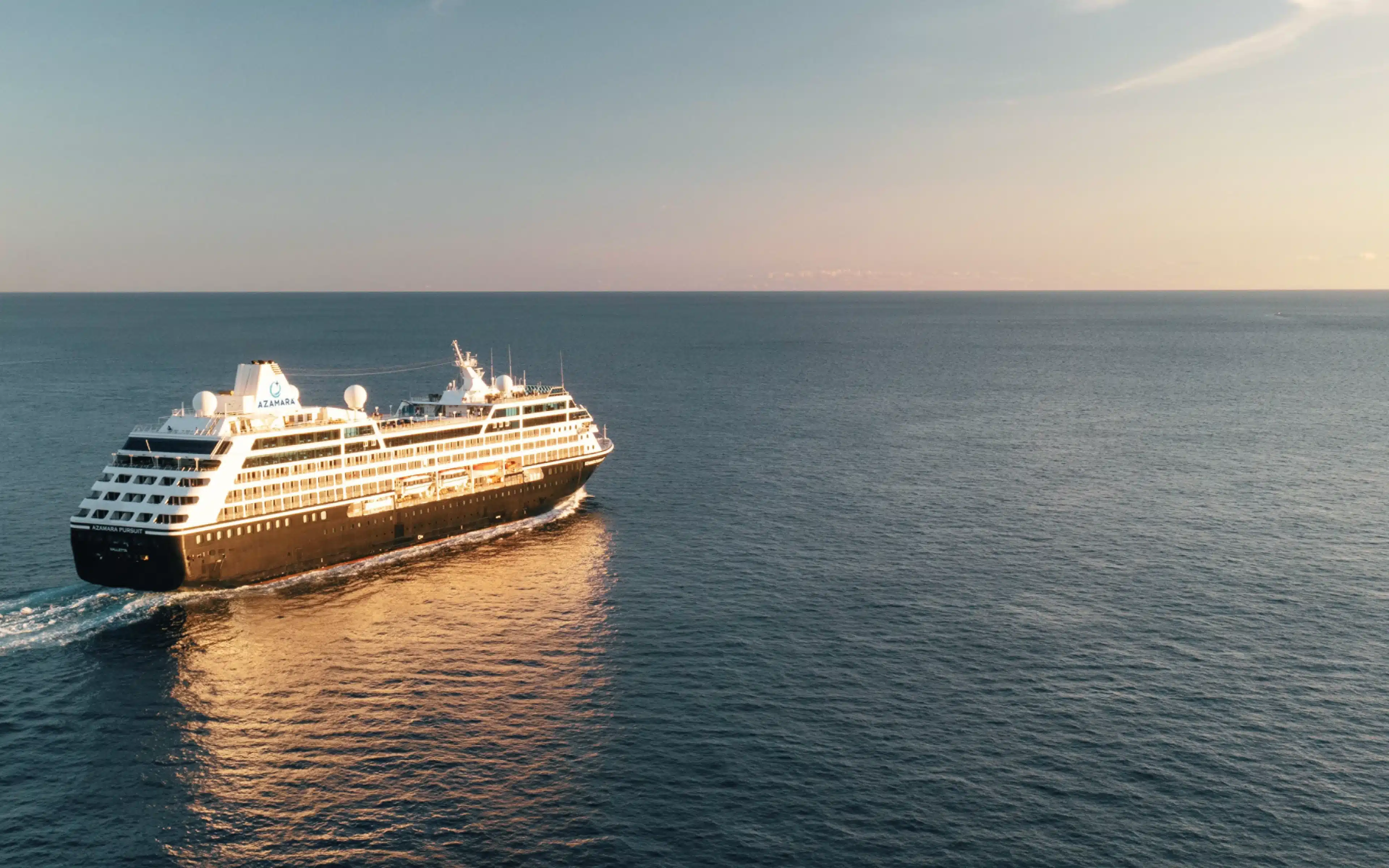 Azamara Pursuit small cruise ship sailing at sunset on calm open ocean.