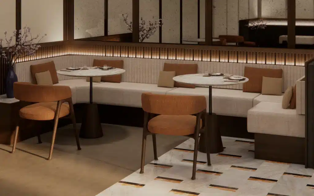 Close-up architectural rendering of curved cream banquette seating in The Bistro aboard Crystal Grace, with marble-topped pedestal tables, amber upholstered side chairs, bronze-toned footrail lighting, and cherry blossom branch in a cobalt vase
