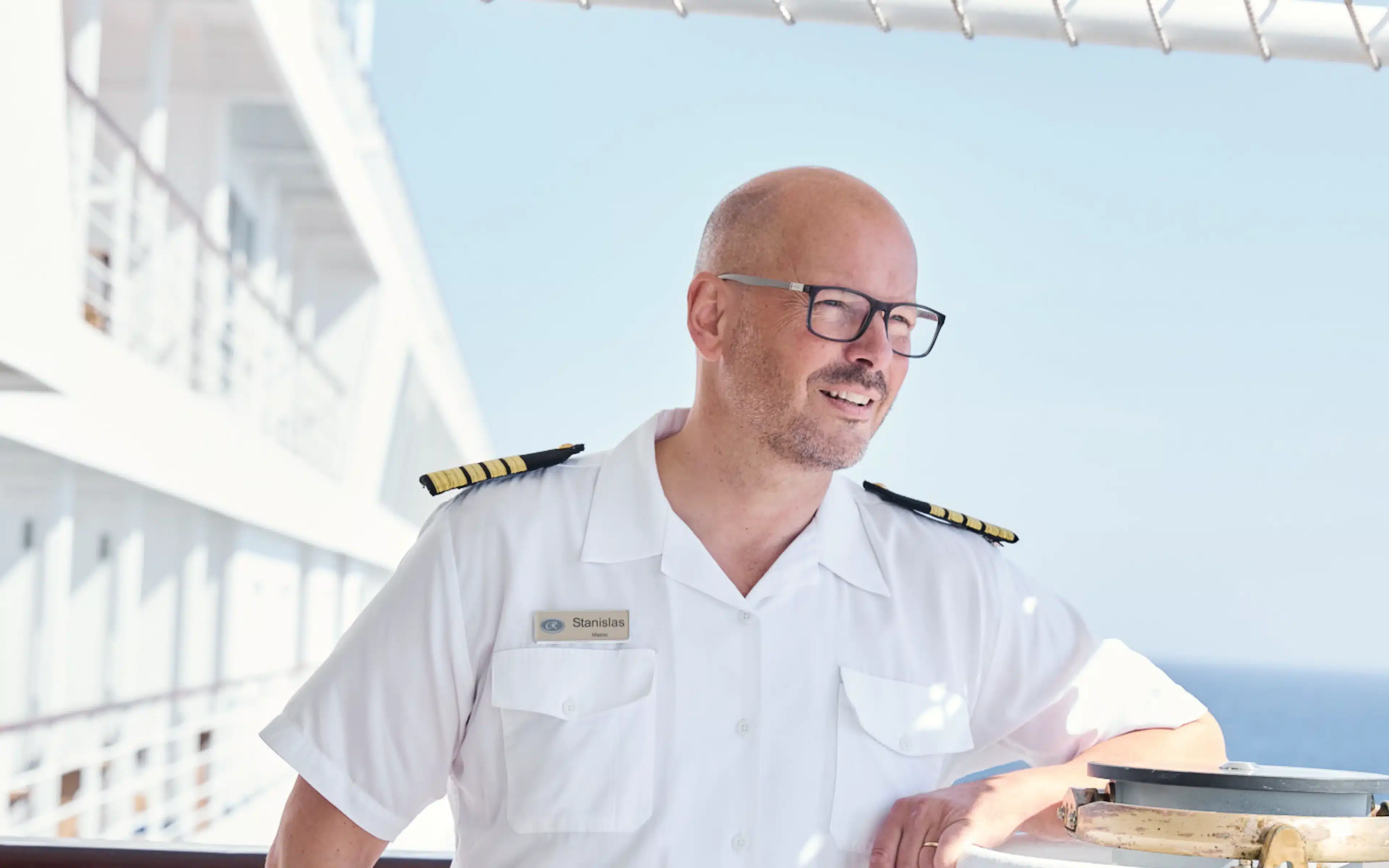 Captain Stanislas in white uniform standing on the open deck of Seven Seas Voyager.
