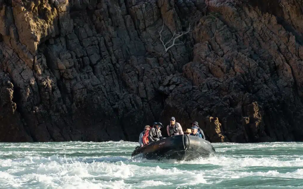 Zodiac tour passengers exploring rugged coastal cliffs