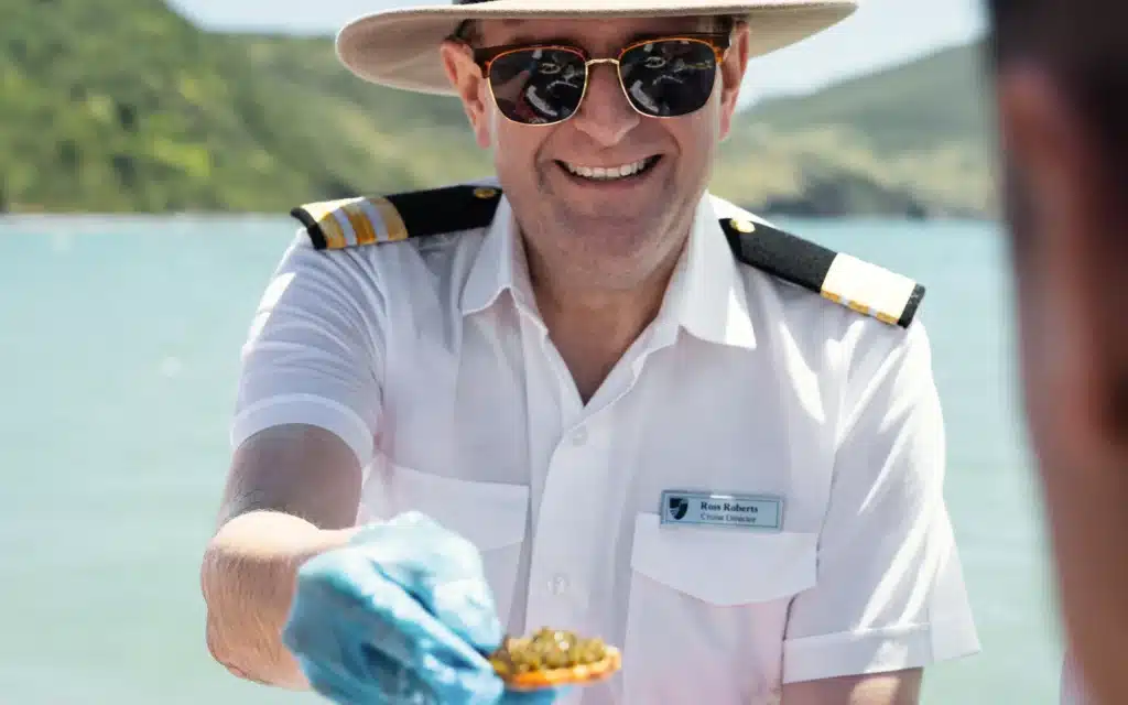 Cruise director in white uniform serving caviar to guests during a tender excursion