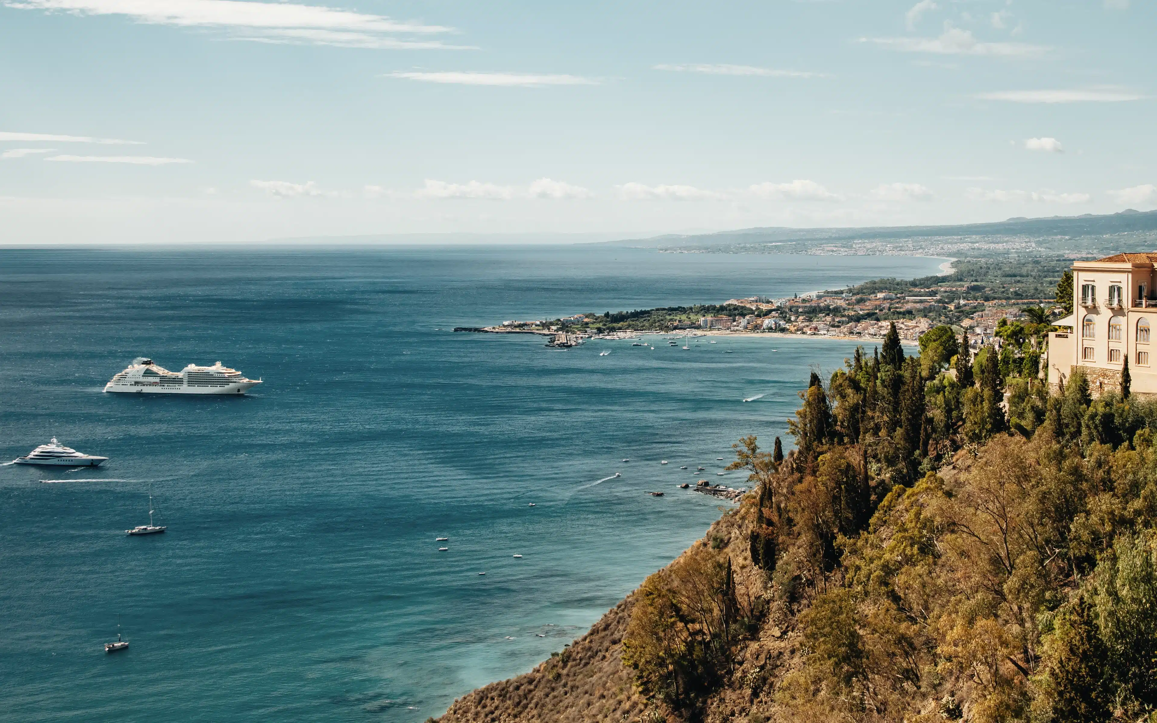 Aerial view of Taormina's coastline with a cruise ship and yachts anchored in turquoise water