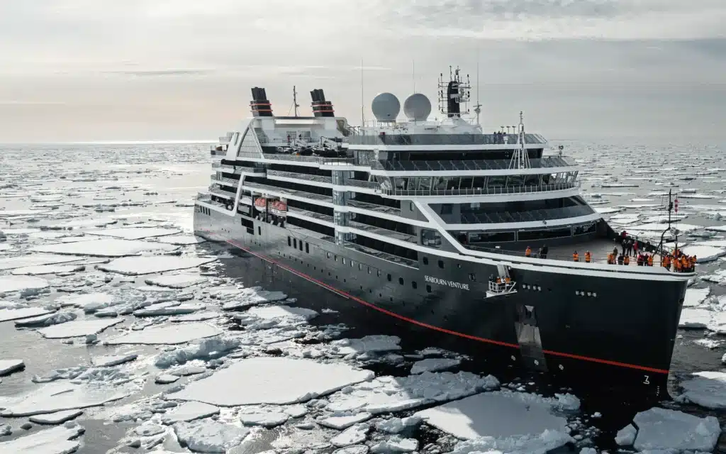 Seabourn Venture expedition ship breaking through ice floes with passengers gathered on deck